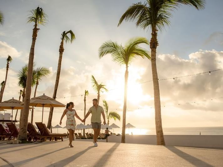 A couple walks hand in hand at sunset under palm trees at Marquis Los Cabos Resort with the ocean in view