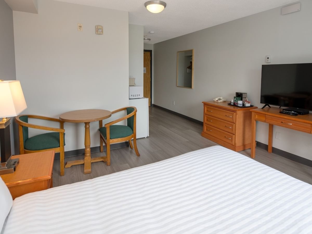 A hotel room with a bed, nightstand, lamp, table, chairs, dresser, TV, and a mini-fridge.