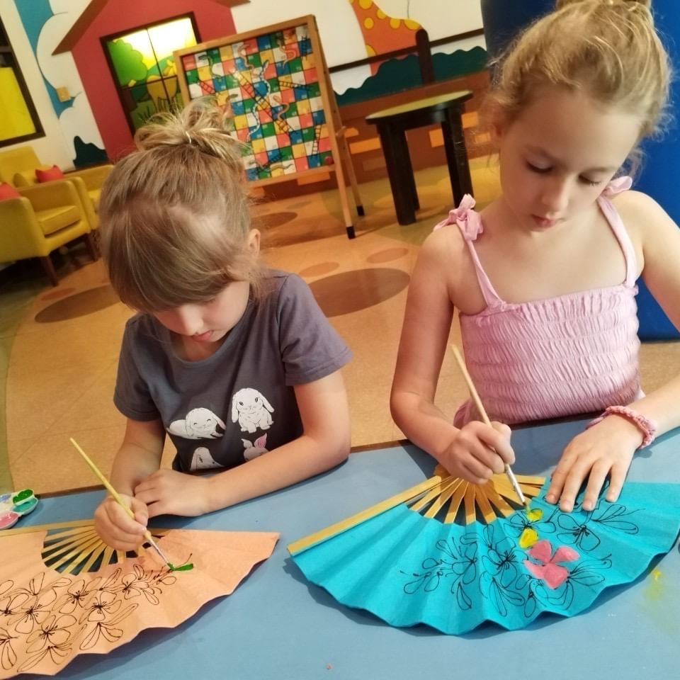 Two happy kids are painting fan in the Kids Club at Paradox Phuket, Karon Beach