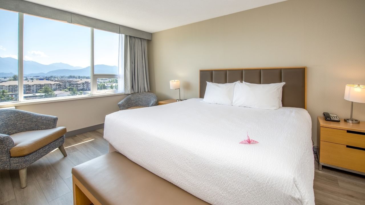 Large bedroom with king-sized bed, lamps, chairs, and a large window with city view.