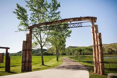 Rustic wooden entrance archway leading to the scenic Ranch at Ucross, with a long driveway and green fields
