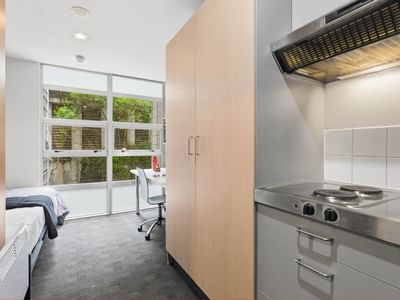 Compact room with bed, desk, and small kitchen area at Student Living Auckland Beach.