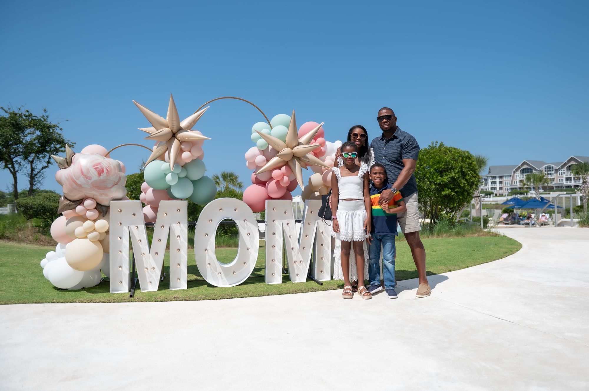 Family of four stands in front of large balloon decoration spelling 