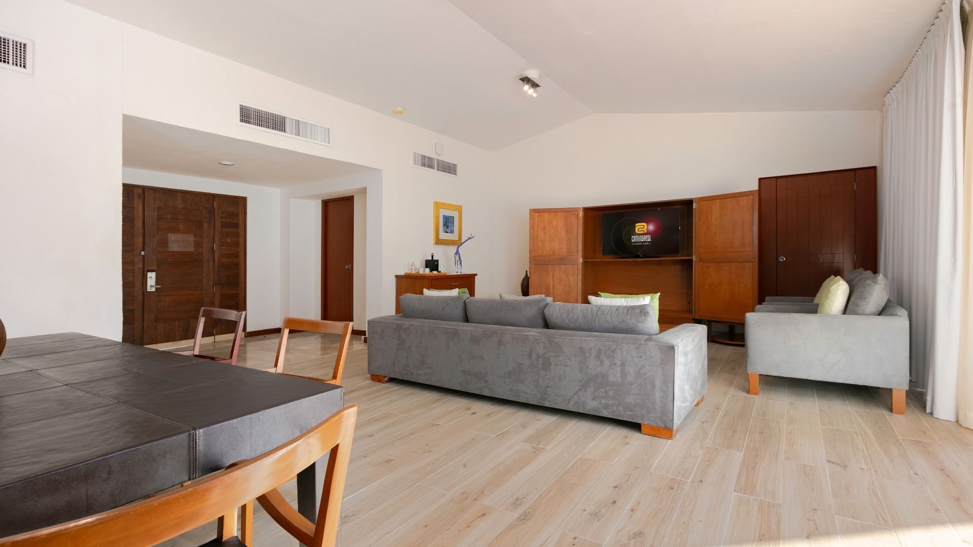 Living area with gray couches, wooden table, and entertainment unit at Camino Real Guadalajara in Zapopan
