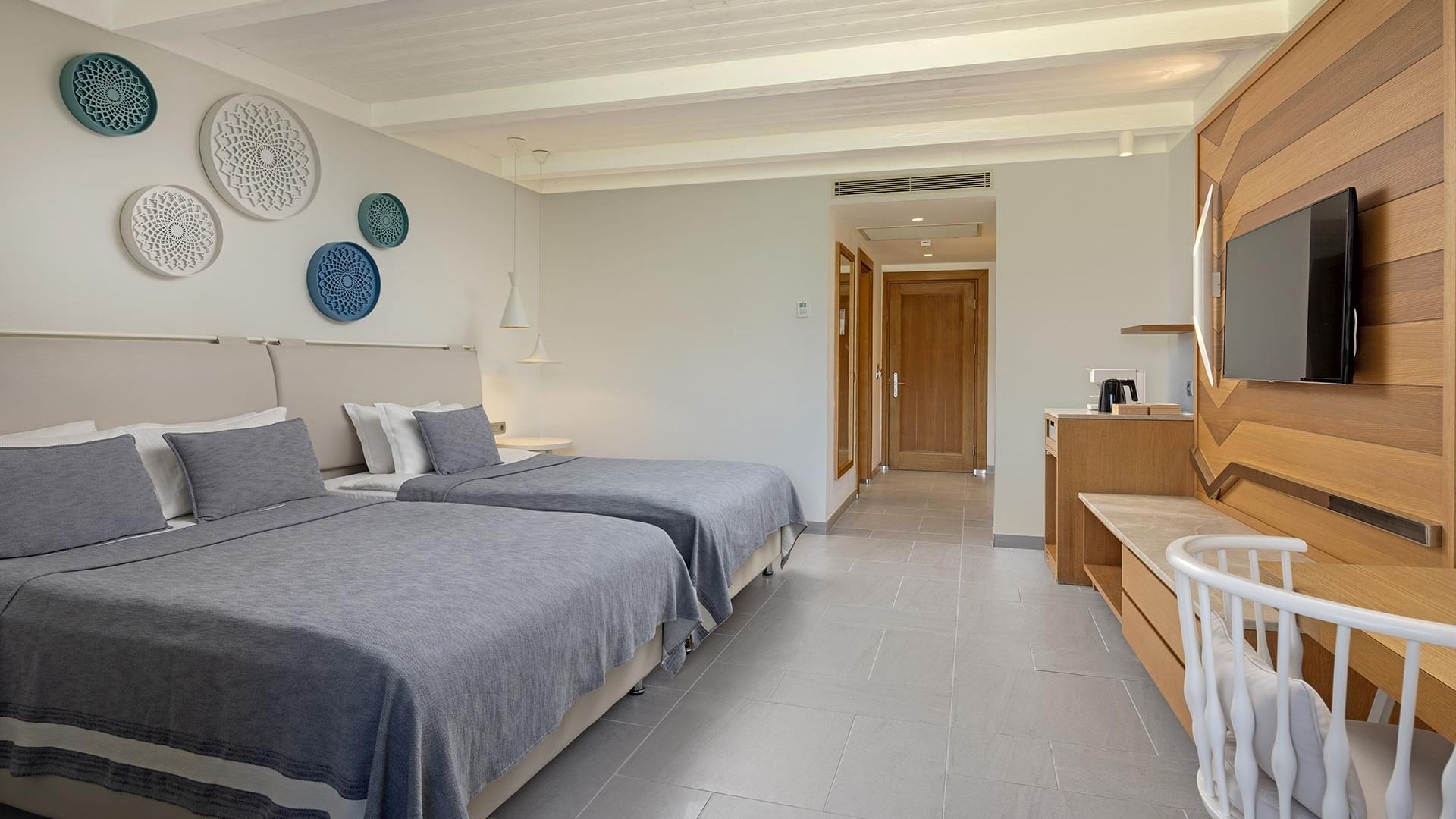 İki yataklı, ahşap masalı, sandalyeli ve duvara monte TV’li standart oda–Titanic Luxury Collection Bodrum.