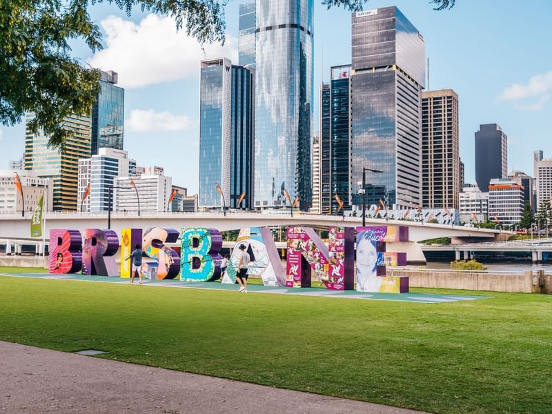 Colorful Brisbane sign with city skyline and green grass at South Bank near Sofitel Brisbane Central