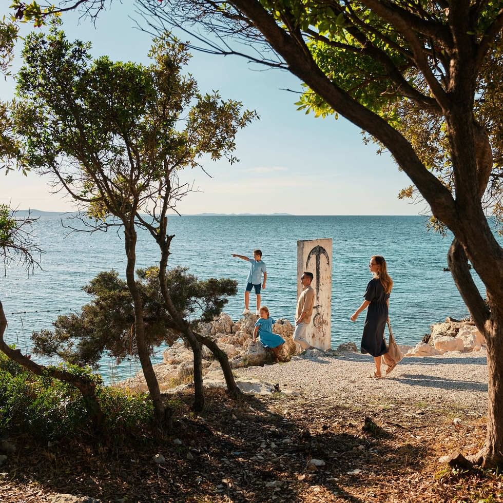 Family enjoying the beach view under trees with an abstract art piece nearby in the Easy Arrival offer.