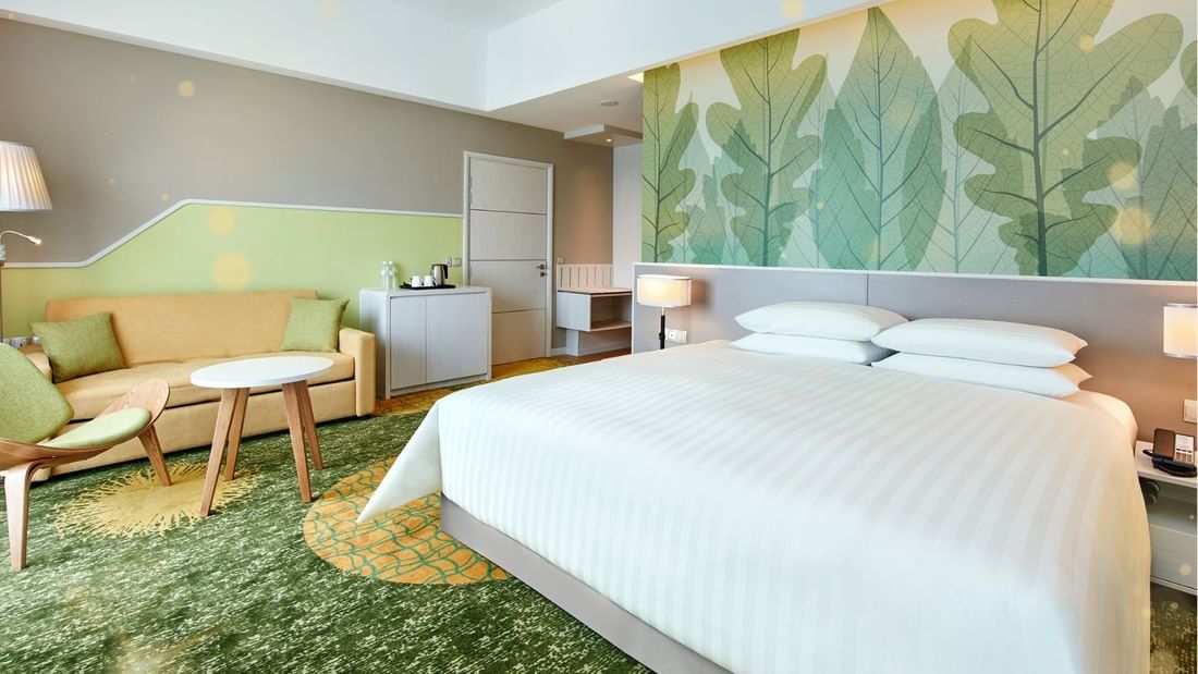 A hotel room with a large bed, couch, chair, table, and a wall with a leaf pattern.