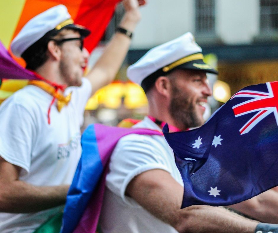 People participating in the Mardi Gras Parade in Sydney, wearing captain's hats while waving rainbow flags