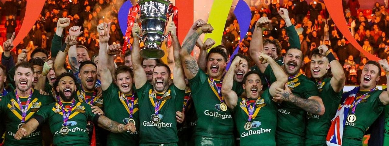 Victorious rugby team in green jerseys celebrating with trophy held high amid cheering crowd and colorful stage backdrop.