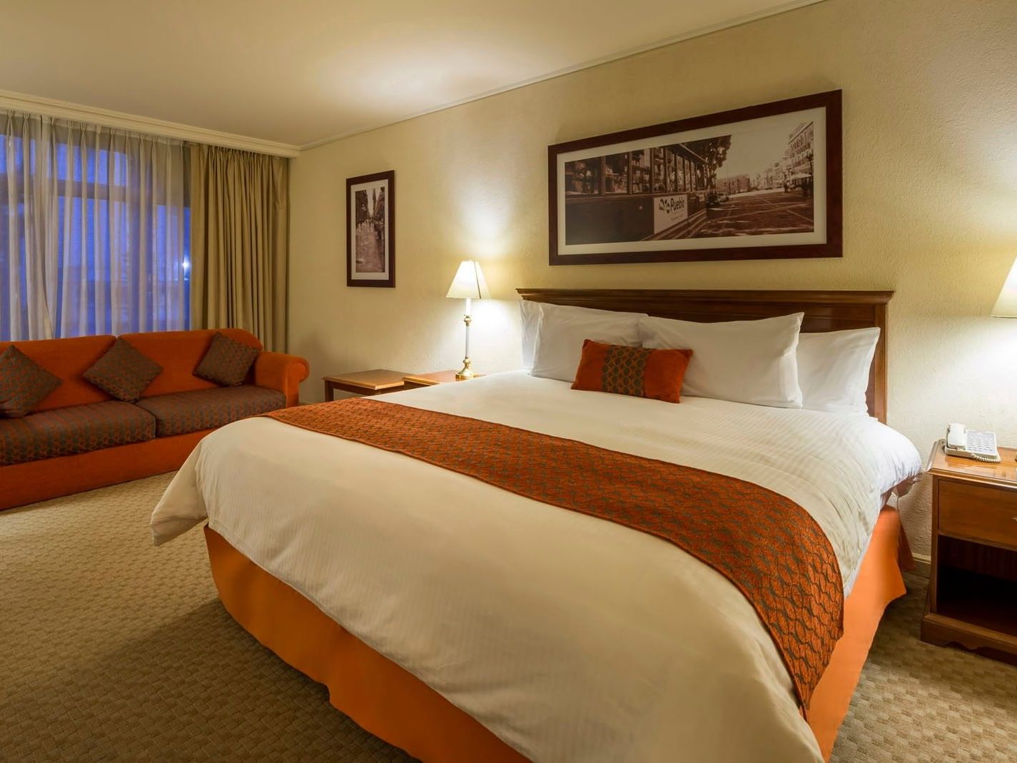 Premium King Camino Real Club featuring a long orange sofa and large framed city artwork at Camino Real Puebla Angelopolis