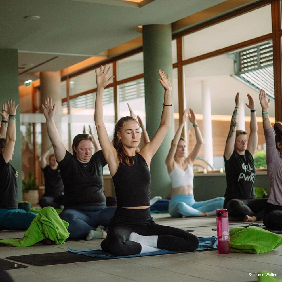 Gruppe von Frauen praktiziert Yoga in einem hellen, luftig Raum mit großen Fenstern.