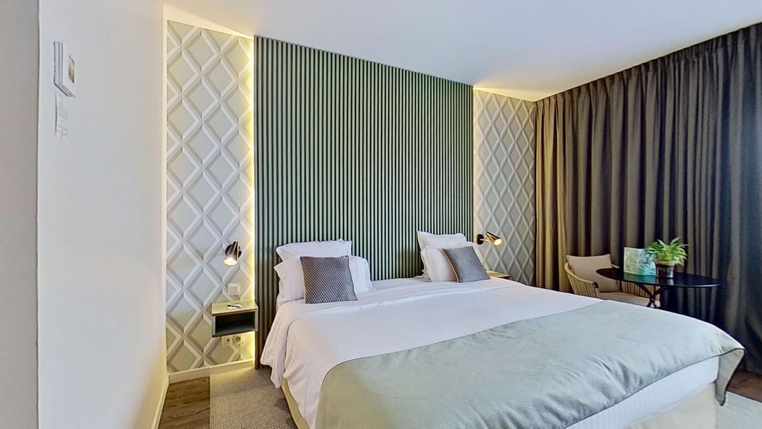 A modern bedroom with a large bed, decorative wall, table, chair, and potted plant.