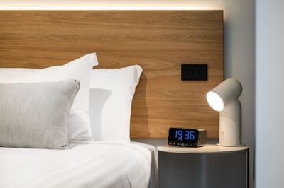 Table lamp & a digital alarm near the bed at Nesuto Docklands