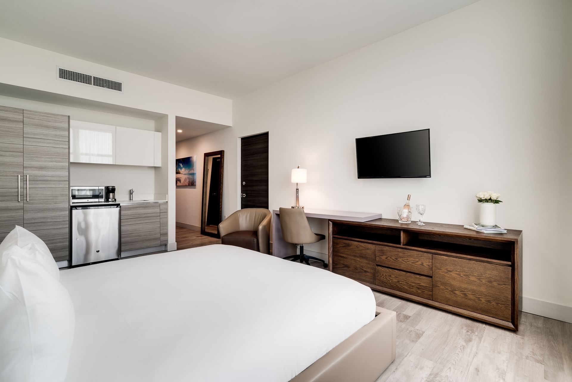 A hotel room with a large bed, kitchenette, desk, and TV