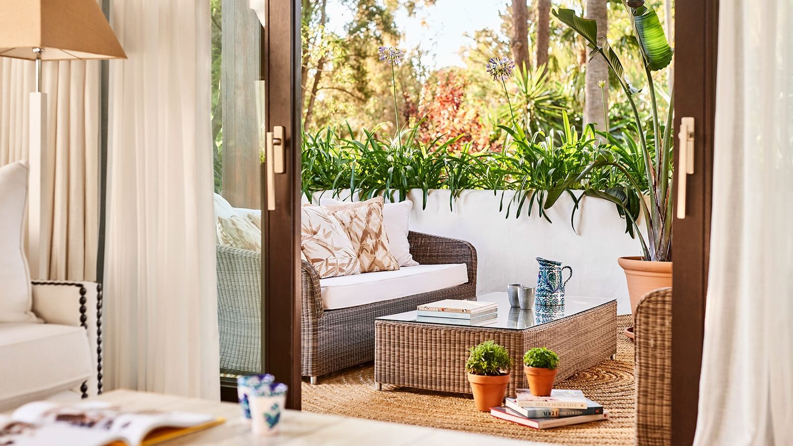 La Concha Suite terrace with wicker seating, a glass coffee table, & lush, exotic plantings at Marbella Club