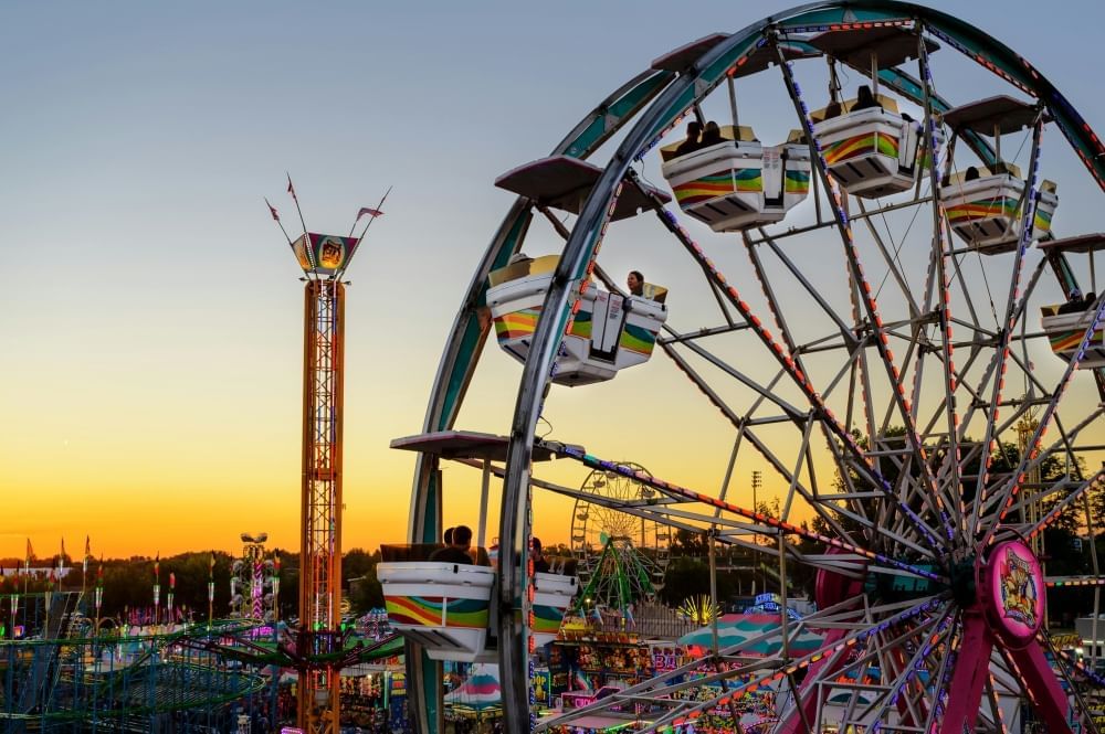 The silhouette of a ferris wheel and other carnival rides at twilight.