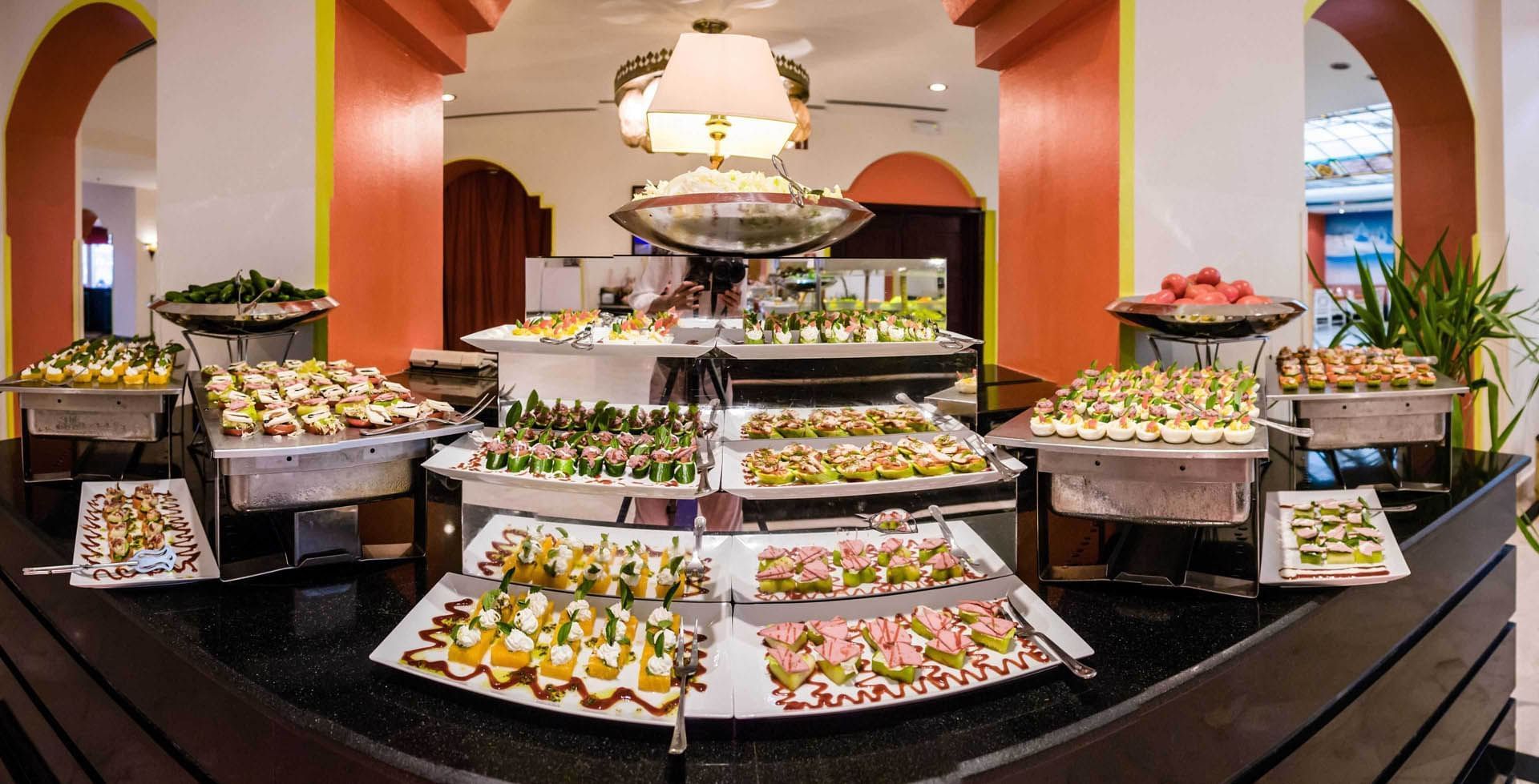 Dessert buffet with colorful pastries, cupcakes & desserts displayed on trays in restaurant at Pickalbatros Golf Beach Resort