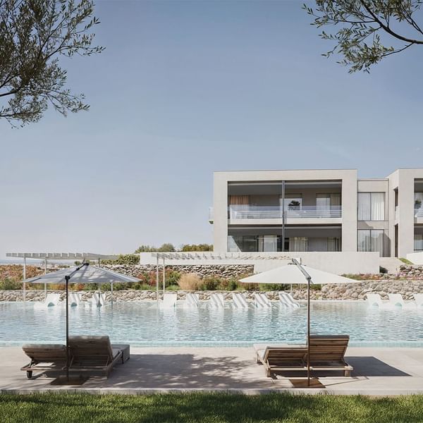 Due lettini sotto due ombrelloni vicino a una piscina e un edificio in stile moderno.