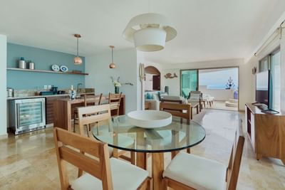 Modern living and dining area with a glass table, wooden chairs, TV, and sliding glass doors to a balcony.