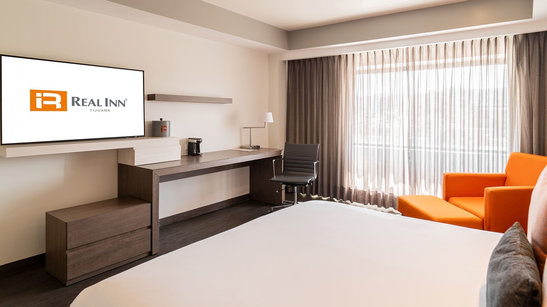 Wall-mounted TV, coffee maker, and work desk by the bed in the King Deluxe Superior Room at Real Inn Tijuana