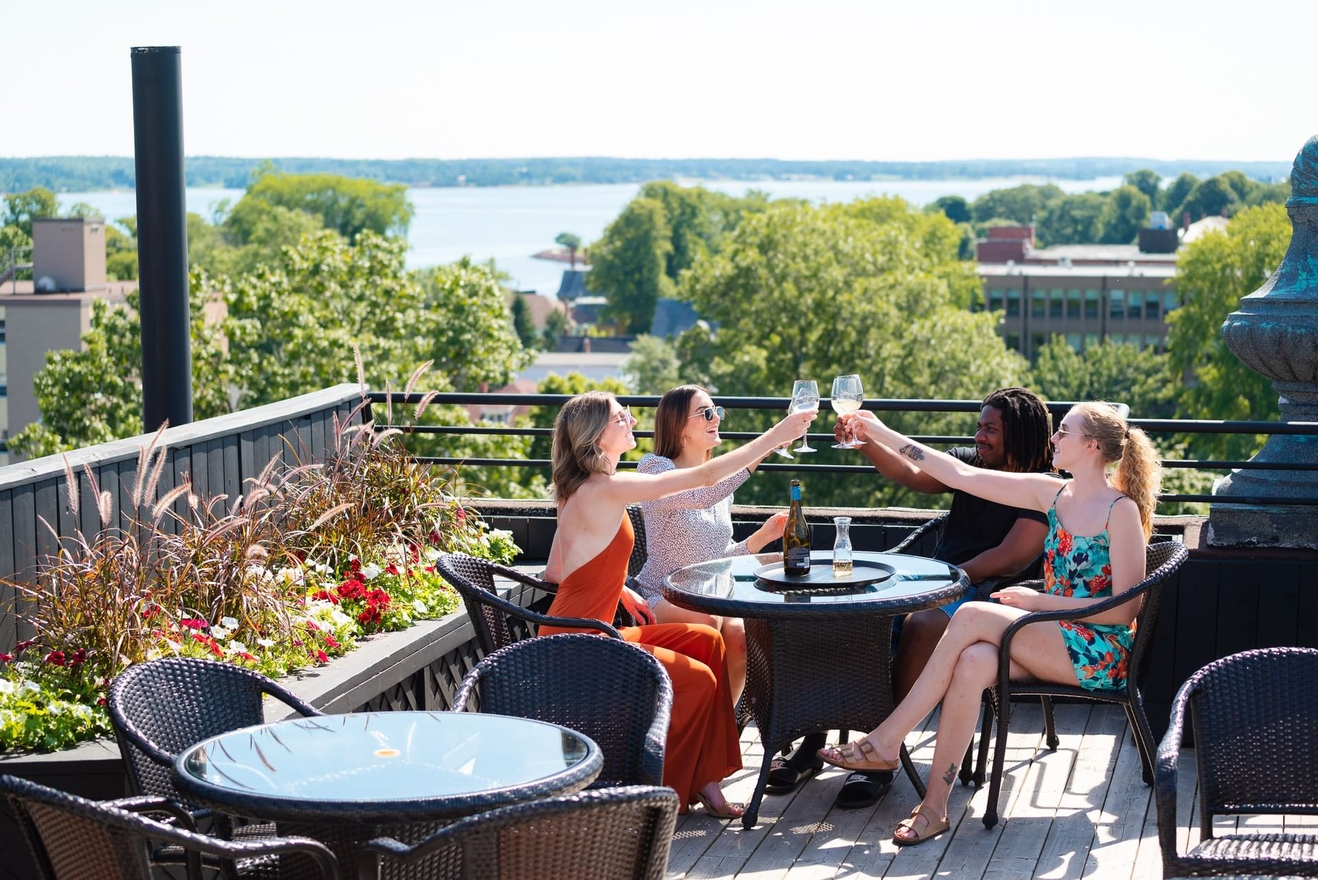 Friends cheering with wine glasses by a table on a rooftop deck under an open sky at Rodd Charlottetown Hotel