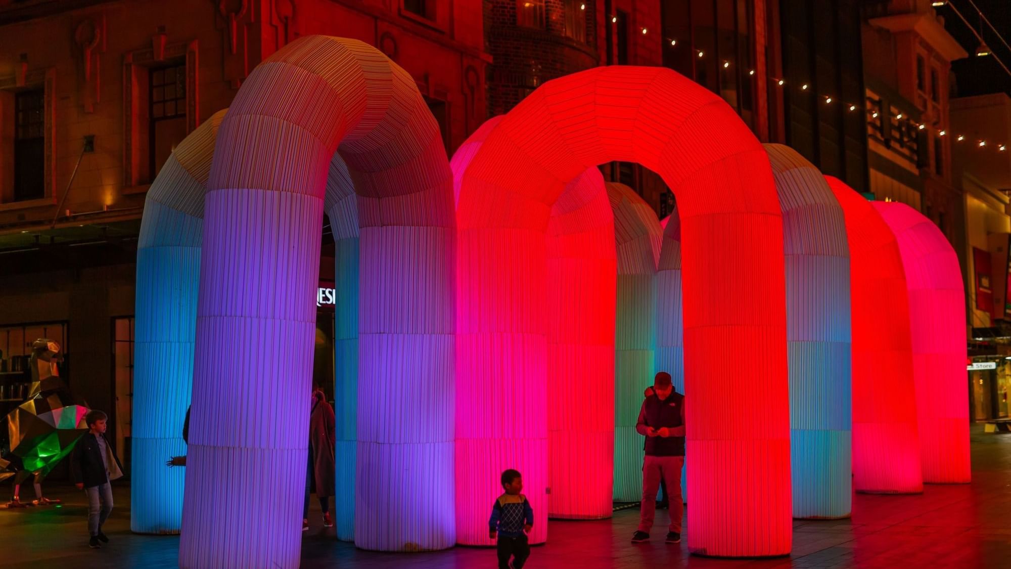Illuminate Adelaide event with colorful arch lights at night in city square.