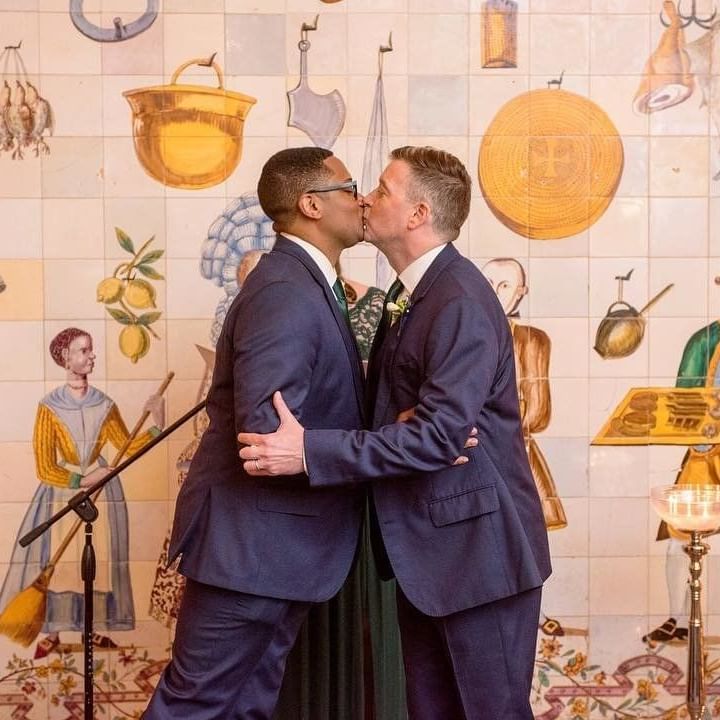 Men kissing in front of a wall with paintings, El Convento