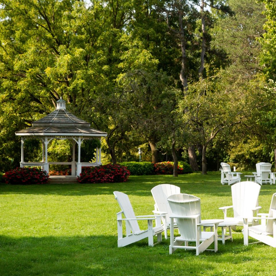 White Adirondack chairs arranged on a grassy lawn near a wooden gazebo at Spencer Hotel & Conference Centre