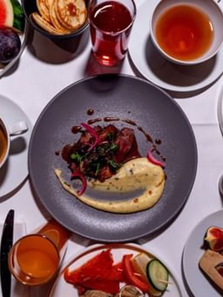 Plates of steak and eggs by cups of coffee and fresh fruit on a white table in Sunday Brunch at Warwick Paris Champs Elysées