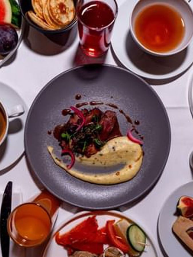 Plates of steak and eggs by cups of coffee and fresh fruit on a white table in Sunday Brunch at Warwick Paris Champs Elysées