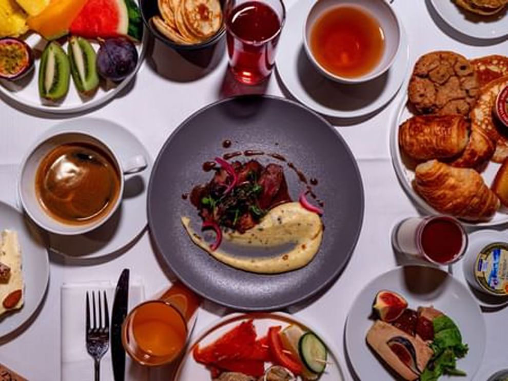 Plates of steak and eggs by cups of coffee and fresh fruit on a white table in Sunday Brunch at Warwick Paris Champs Elysées