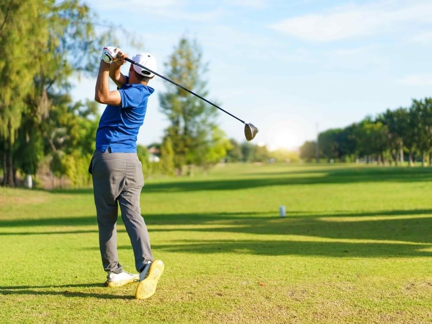 Man swinging a golf club on a green field showcasing Golf Packages.