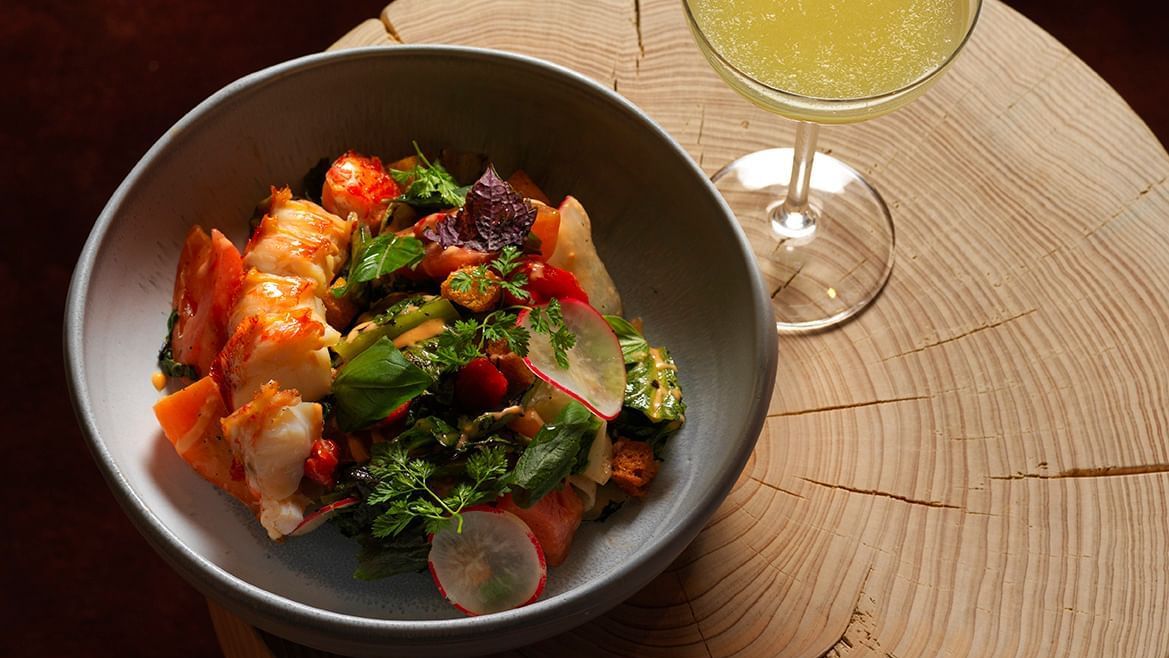 Bowl of seafood salad with a glass of green cocktail drink on a wooden table.