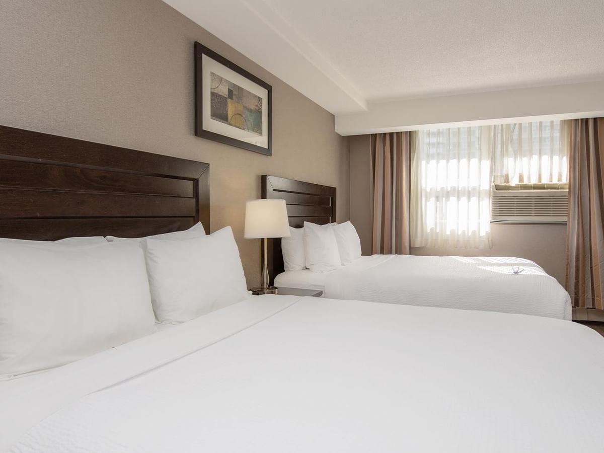 Two  queen beds with wooden headboards in a hotel room