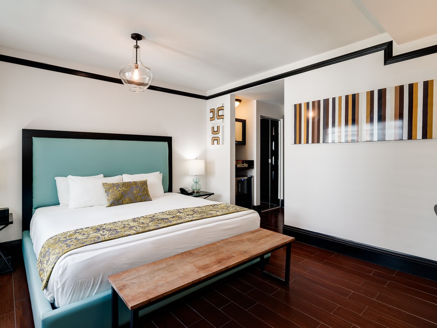 A bedroom with a large bed, wooden bench, striped wall art, and a wooden floor.