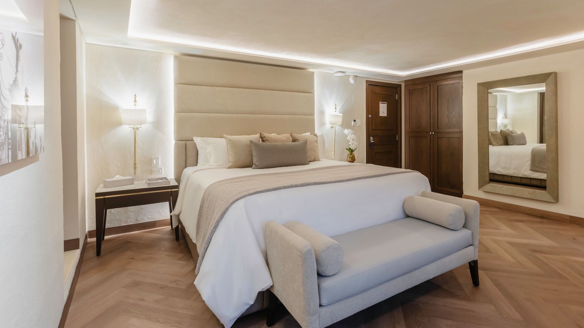 King Deluxe room featuring a white cozy bed, a grey bench, and warm recessed lighting at Quinta Real Puebla