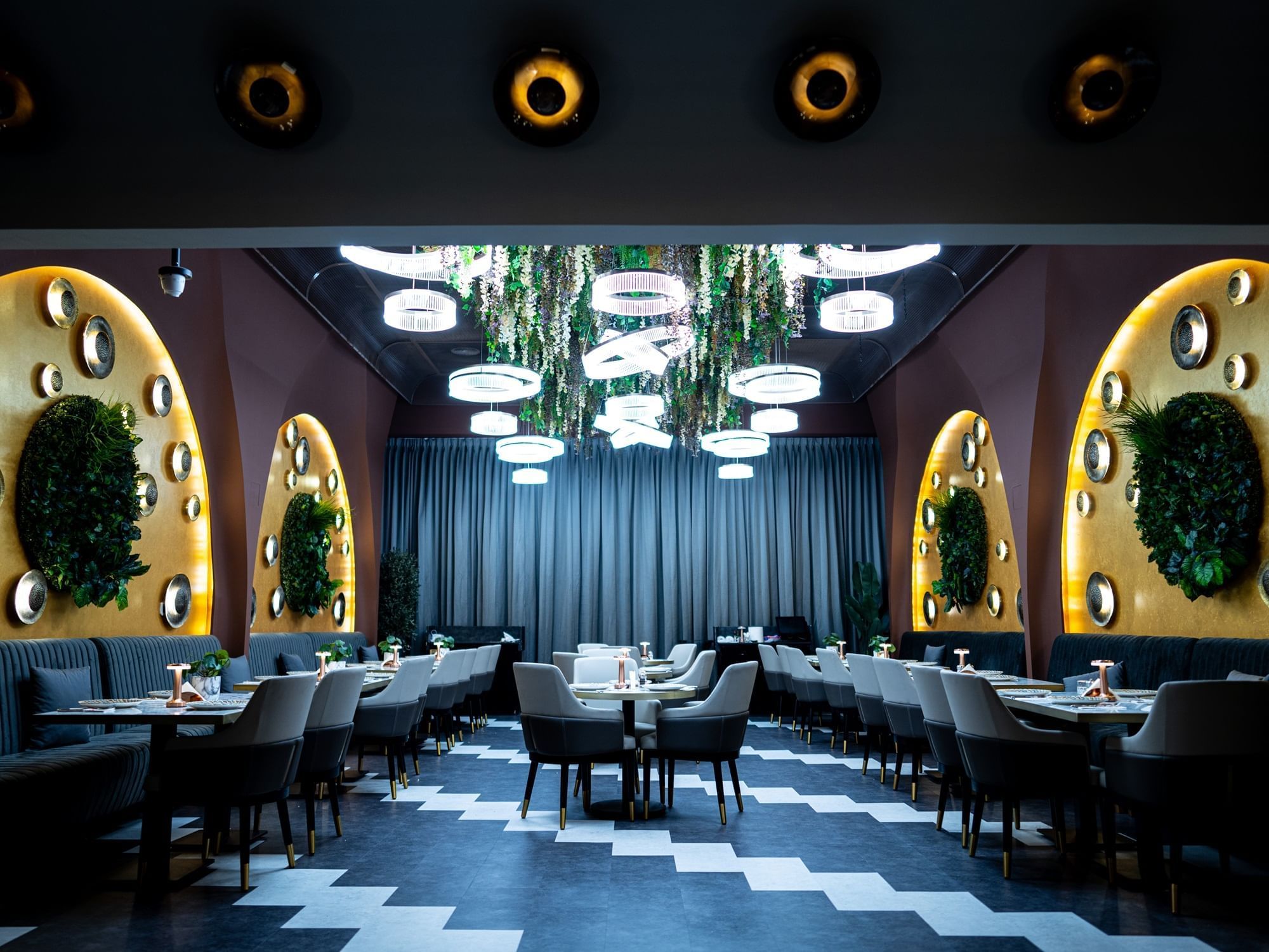 Restaurant and Lounge interior with golden wall accents, greenery ceiling, and ambient lighting at DAMAC Maison Aykon City