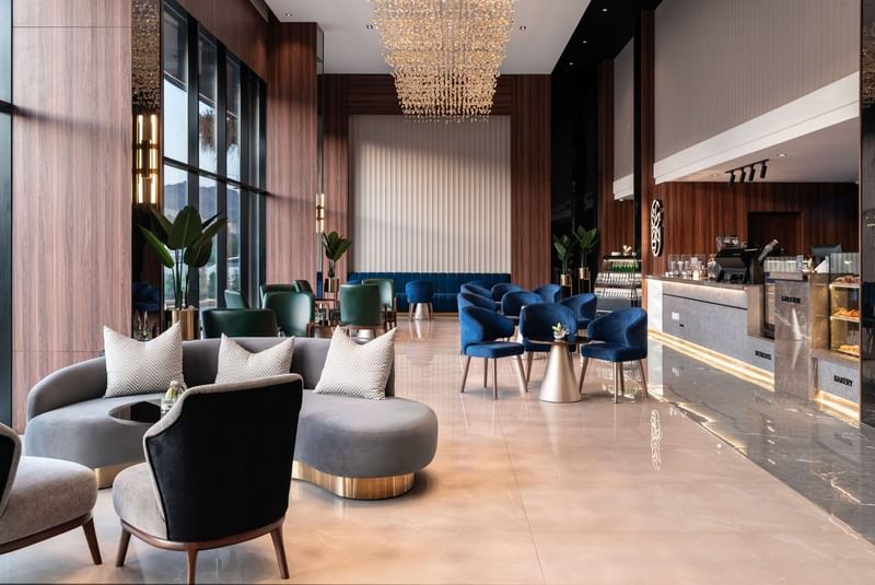 Plush blue and grey sofas by a gold-based table under a large chandelier in Khva Cafe at Warwick Al Taif Hotel