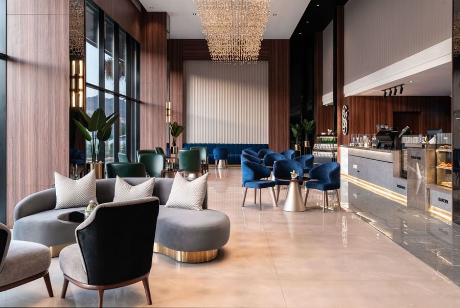 Plush blue and grey sofas by a gold-based table under a large chandelier in Khva Cafe at Warwick Al Taif Hotel