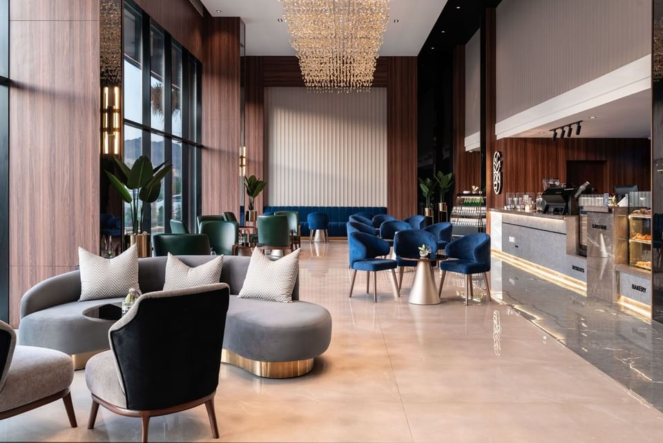 Plush blue and grey sofas by a gold-based table under a large chandelier in Khva Cafe at Warwick Al Taif Hotel