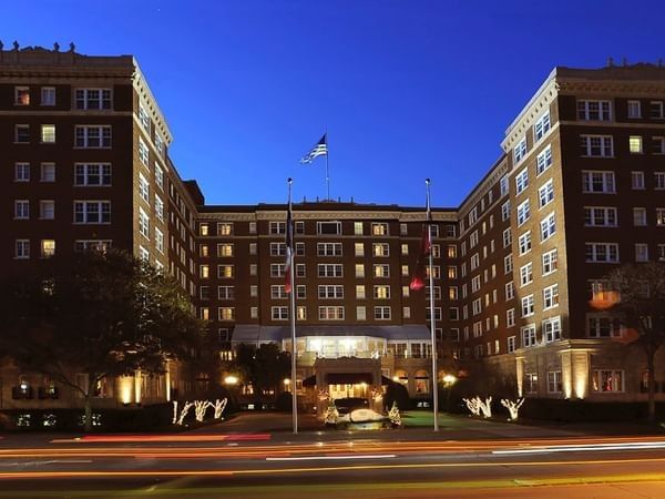 Exterior view of the entrance by lit trees under a twilight sky at Warwick Melrose Dallas