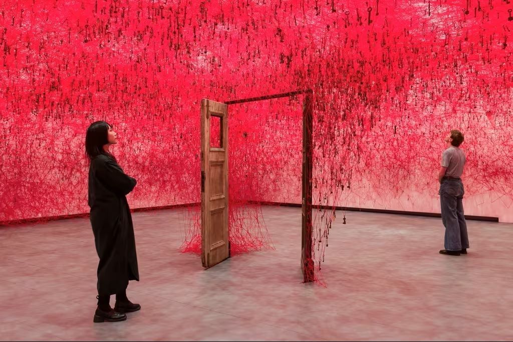 Visitantes a admirar uma instalação artística imersiva composta por milhares de fios vermelhos e chaves suspensos, perto do Hotel The Londoner