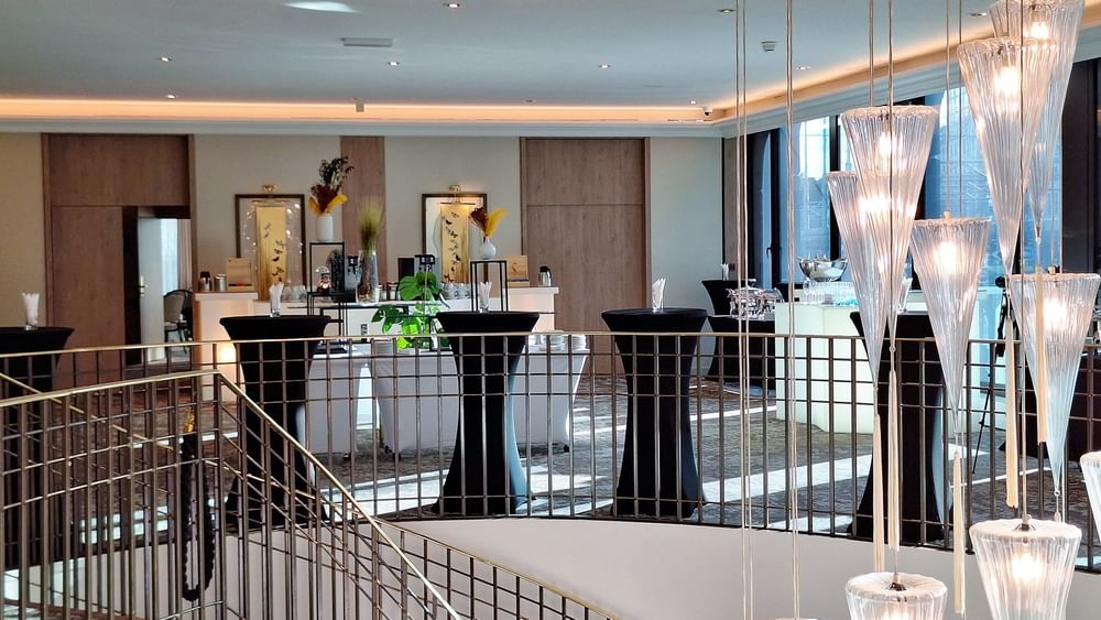 Foyer Mezzanine with black bistro tables by a metal railing under glass pendant lights at Warwick Geneva