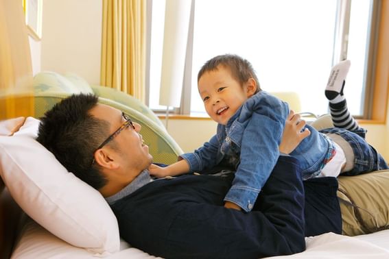 A kid playing with his father on a bed in a room at Grand Park Otaru