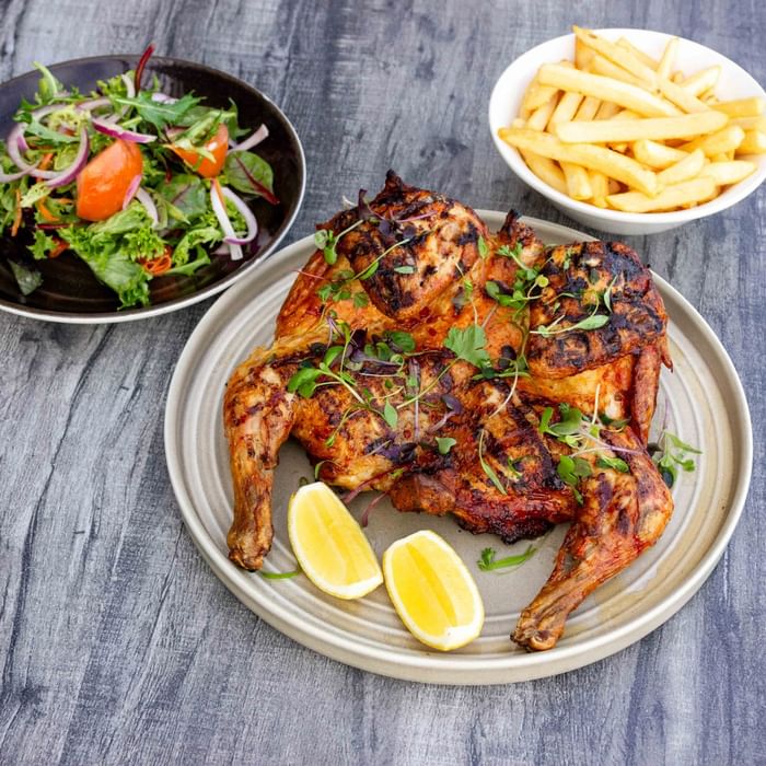 Grilled chicken, lemon wedges, salad, and fries on a wooden surface.