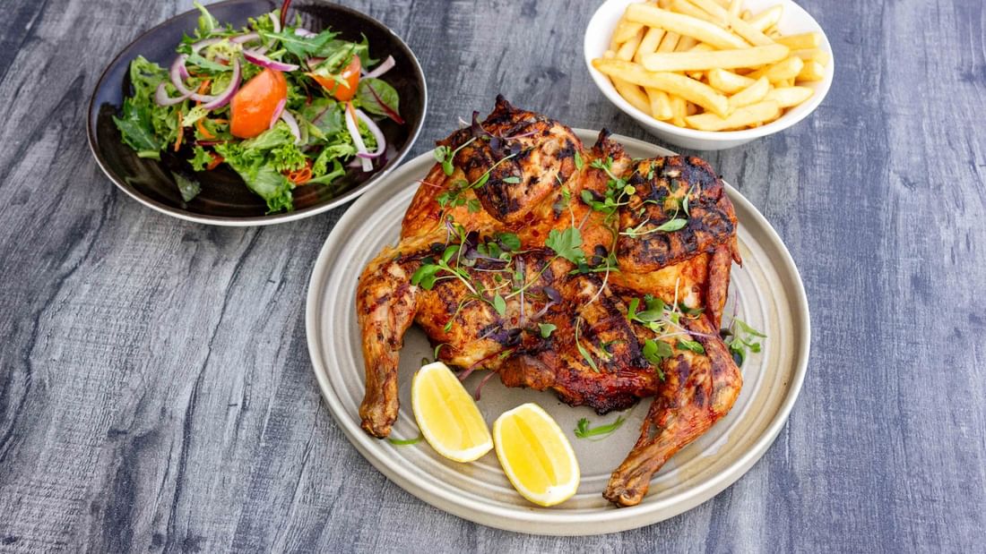 A plate of grilled chicken with lemon slices, alongside a salad and fries on a blue wooden table.