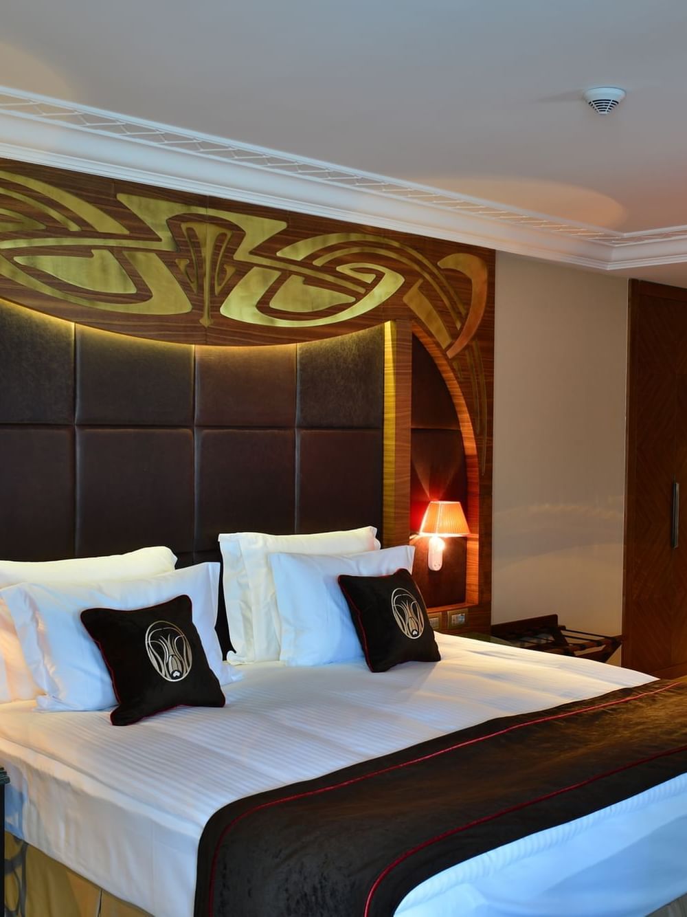 Bed with brown pillows by a green marble table under a gold ornate headboard in Executive Room at Warwick Ankara