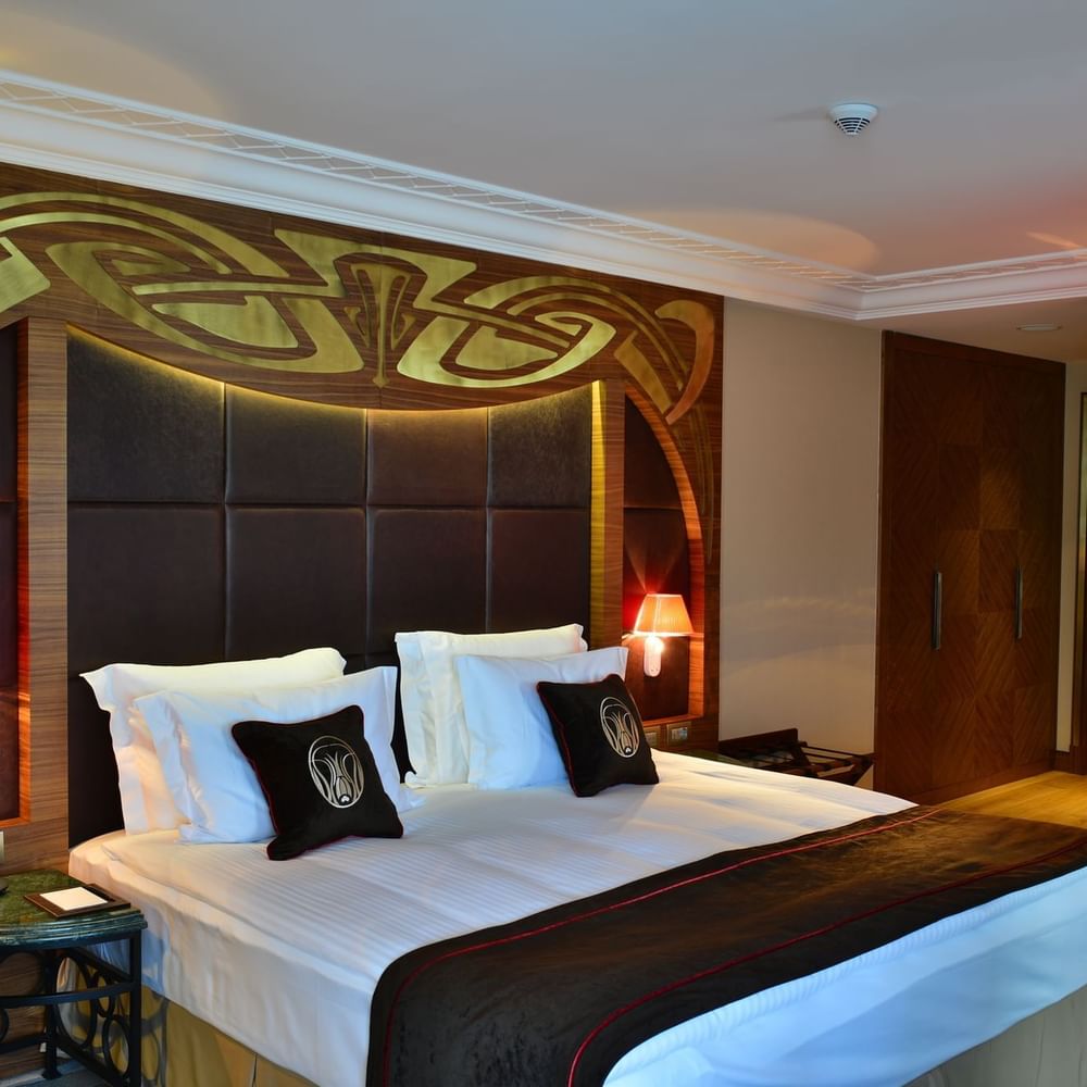 Bed with brown pillows by a green marble table under a gold ornate headboard in Executive Room at Warwick Ankara
