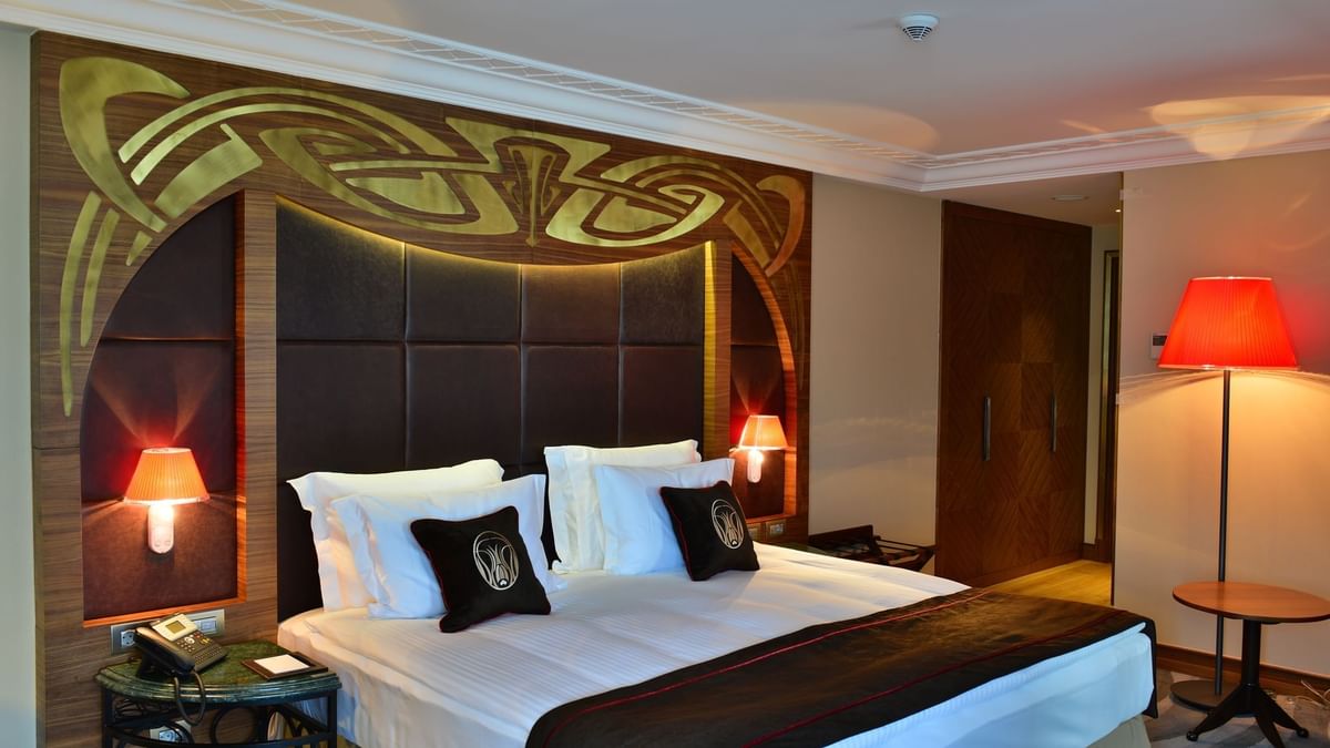 Bed with brown pillows by a green marble table under a gold ornate headboard in Executive Room at Warwick Ankara